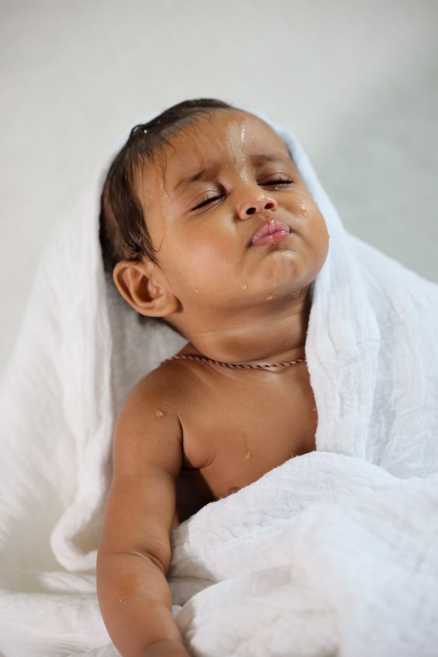 Cute baby wrapped in a white towel with eyes closed, enjoying a moment after a bath.